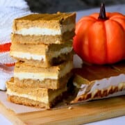 Low carb pumpkin spice cheesecake bars stacked on top of each other next to a pumpkin.