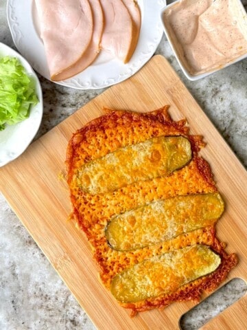 Low carb viral pickle sandwich wrap on a cutting board next to lettuce, turkey slices and a sauce.