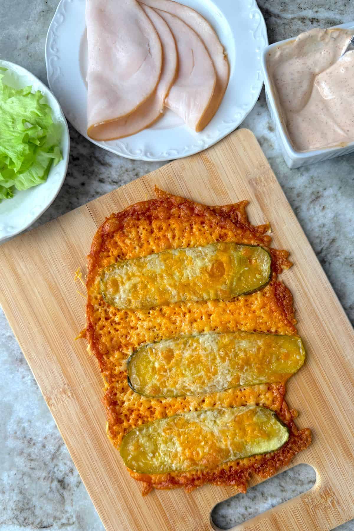 Low carb viral pickle sandwich wrap on a cutting board next to lettuce, turkey slices and a sauce.