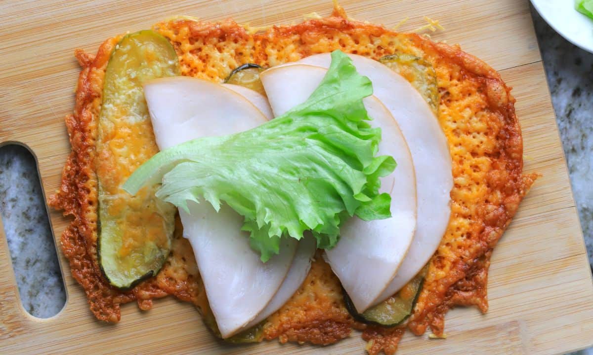Low carb viral pickle sandwich wrap on a cutting board topped with lettuce, turkey slices and a sauce.