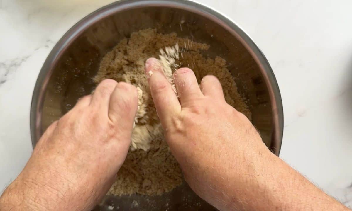 Using hands to mix the butter into the dry ingredients.