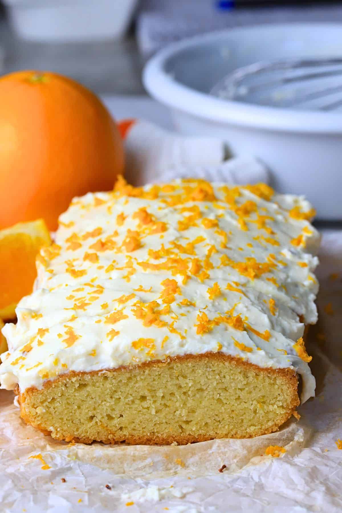 Low carb orange loaf cake on parchment paper next to an orange.