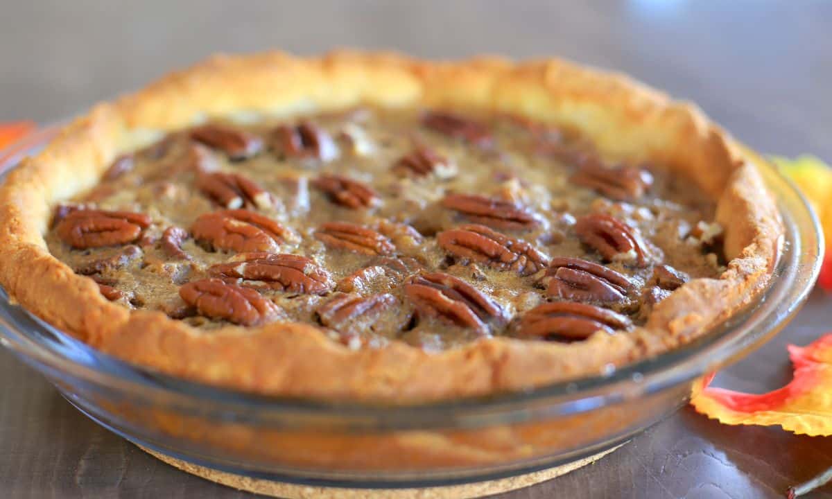 Sugar free pecan pie in a pie dish next to some fall colored leaves.