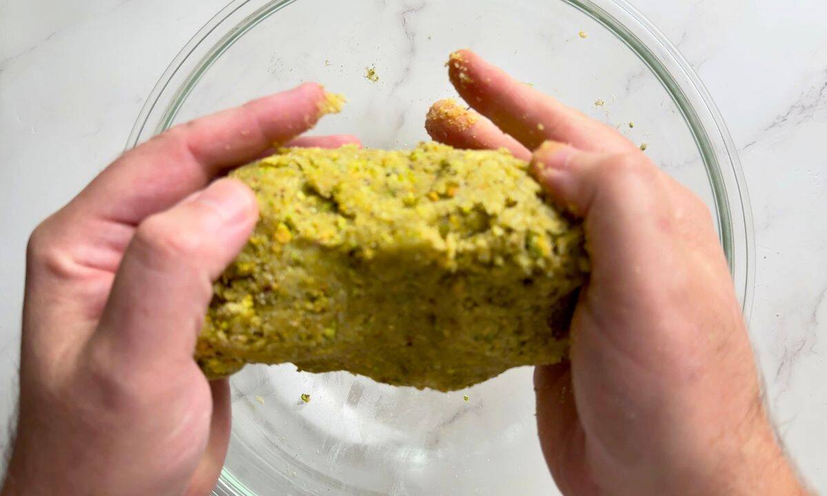 Two hands holding ball of cookie dough over a bowl.