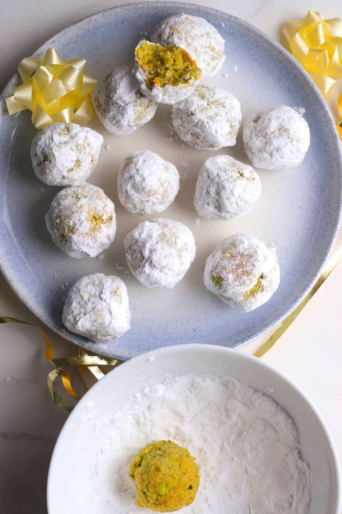 Low carb pistachio snowball cookies on a plate with one cookie in a bowl with powdered sweetener.