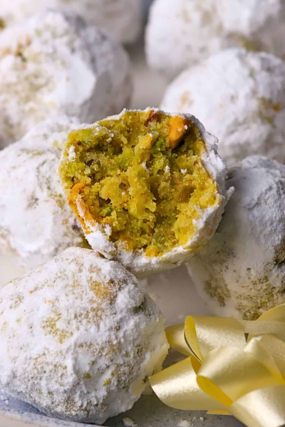Low carb pistachio snowball cookies on a plate with one cookie with a bite in it.