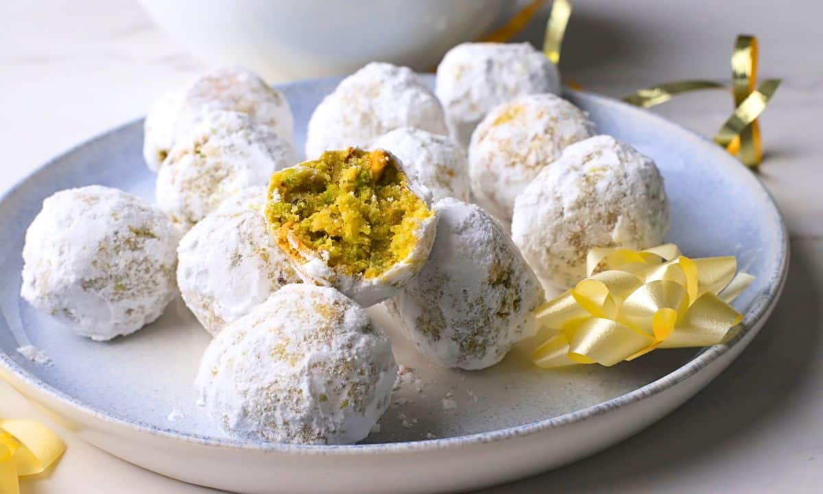 Low carb pistachio snowball cookies on a plate with one cookie with a bite in it.