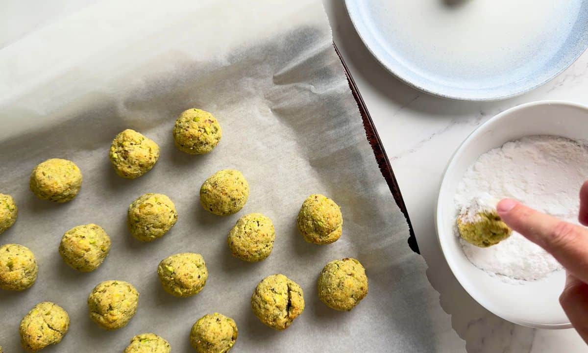 Rolling the baked pistachio cookies in the powdered sweetener.