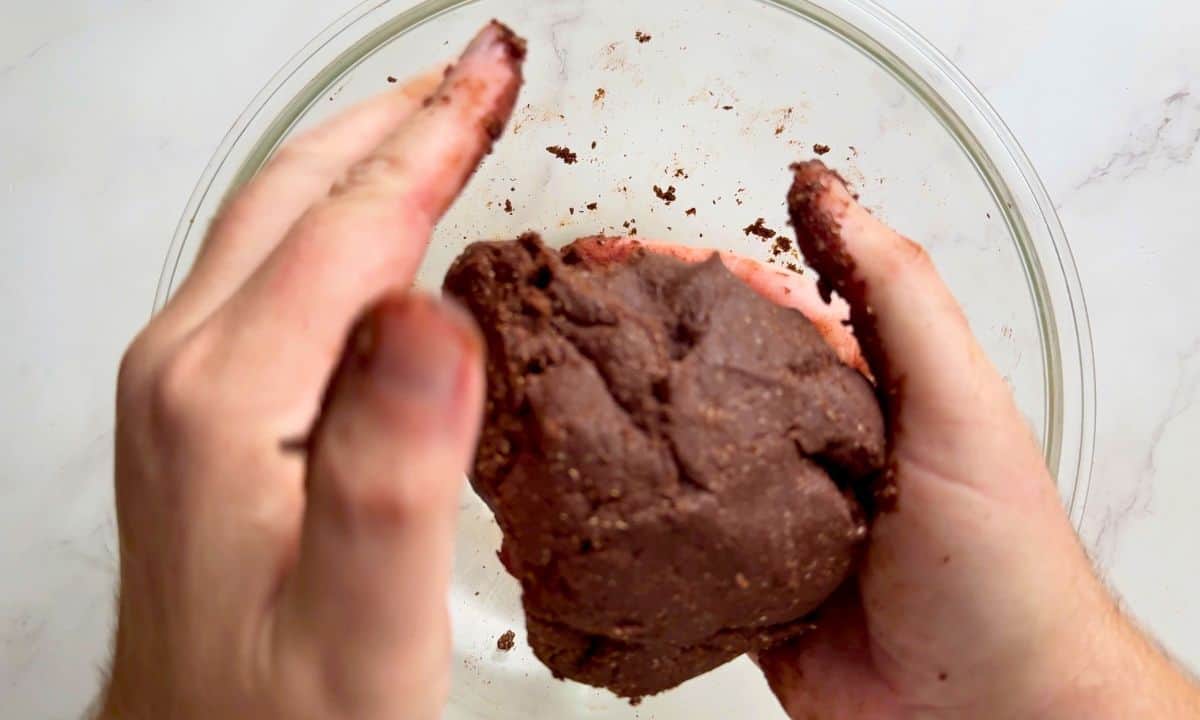 Cookie dough ball in hands over a bowl.