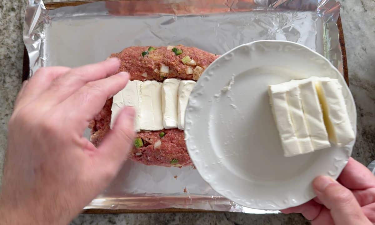 Placing the cream cheese in the well of the meatloaf.