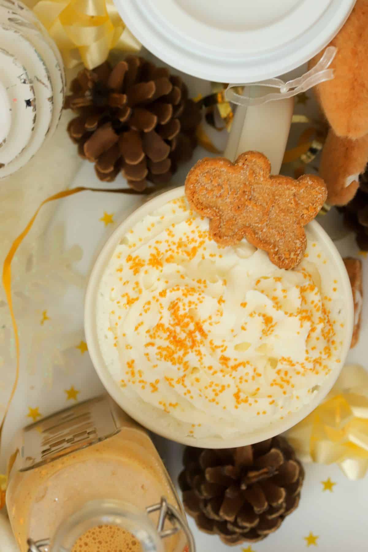 Coffee mug topped with whipped cream and a gingerbread man cookie on top.