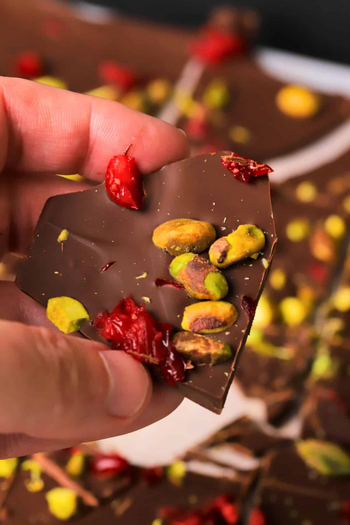 Holding a piece of the low carb pistachio cranberry chocolate bark.