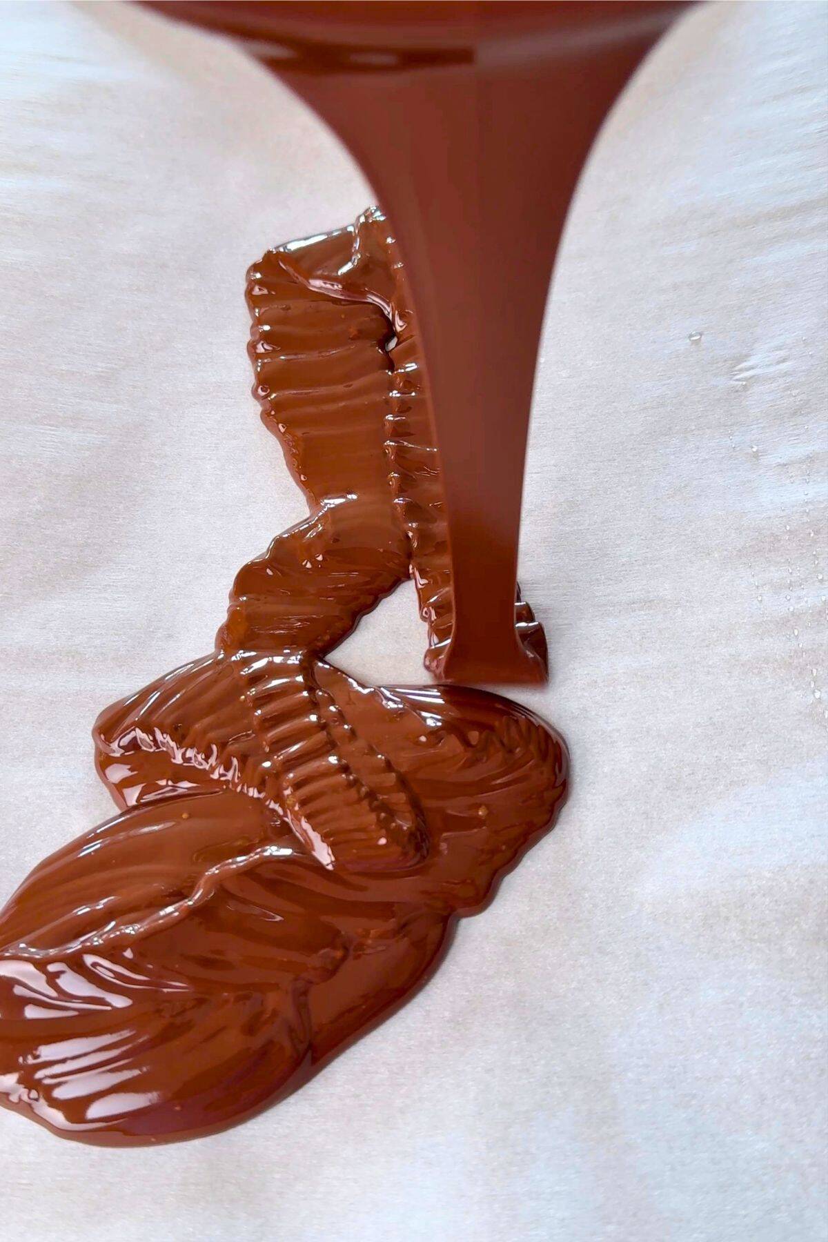 Pouring chocolate on a parchment lined baking sheet.