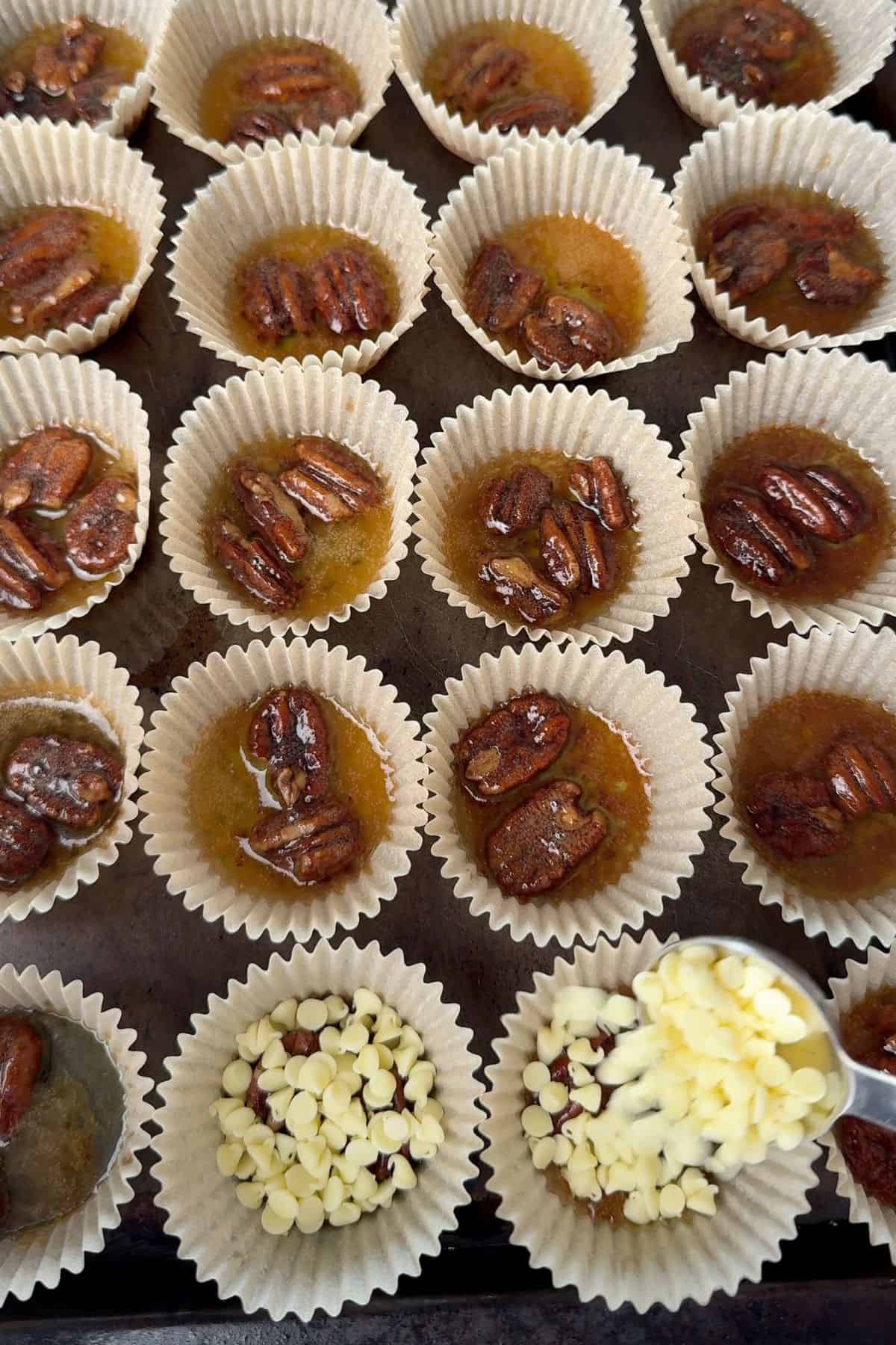 Adding the sugar free white chocolate chips to the buttery pecans in muffin liners.