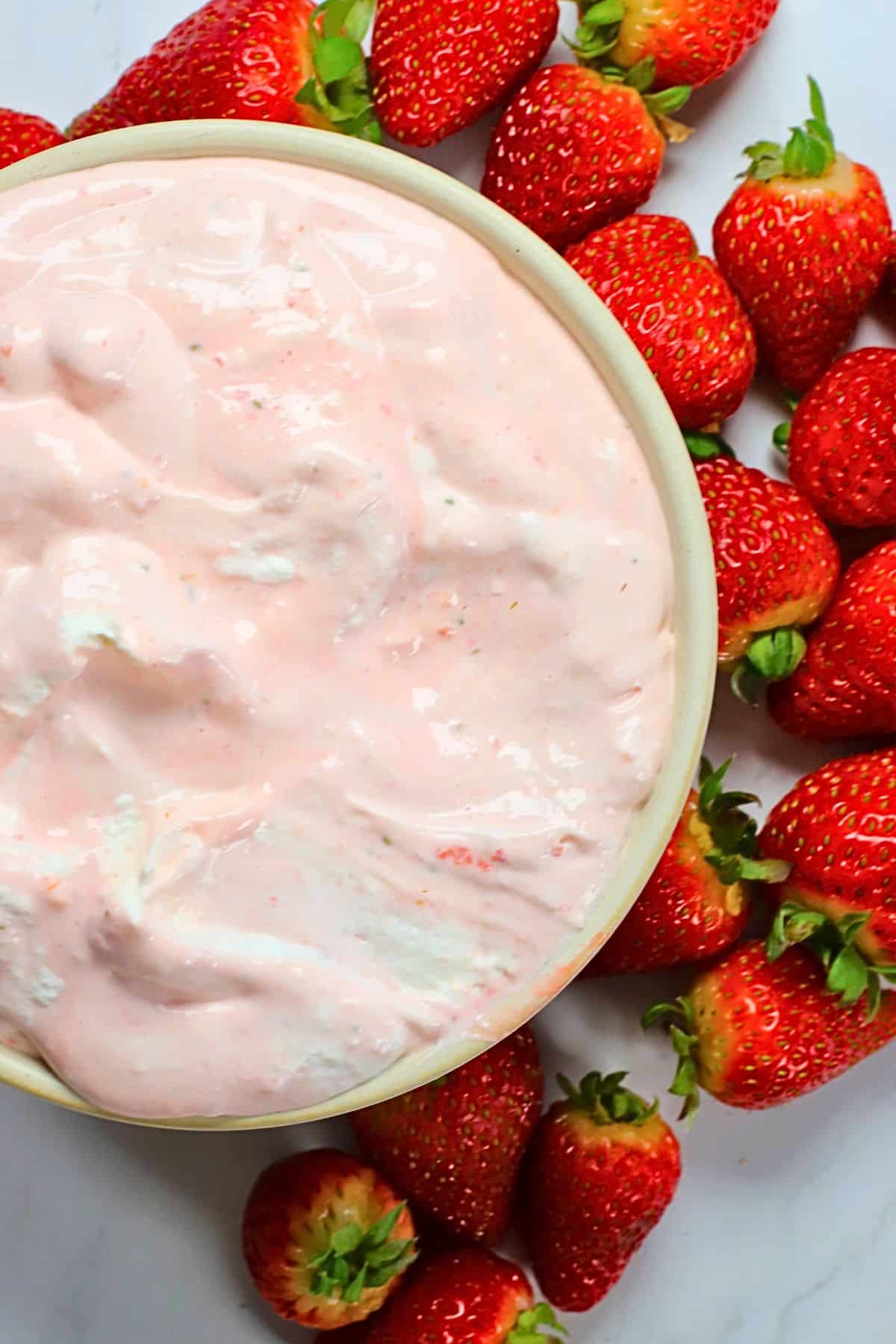 High protein strawberry cheesecake fluff in a bowl and more strawberries surrounding the bowl.