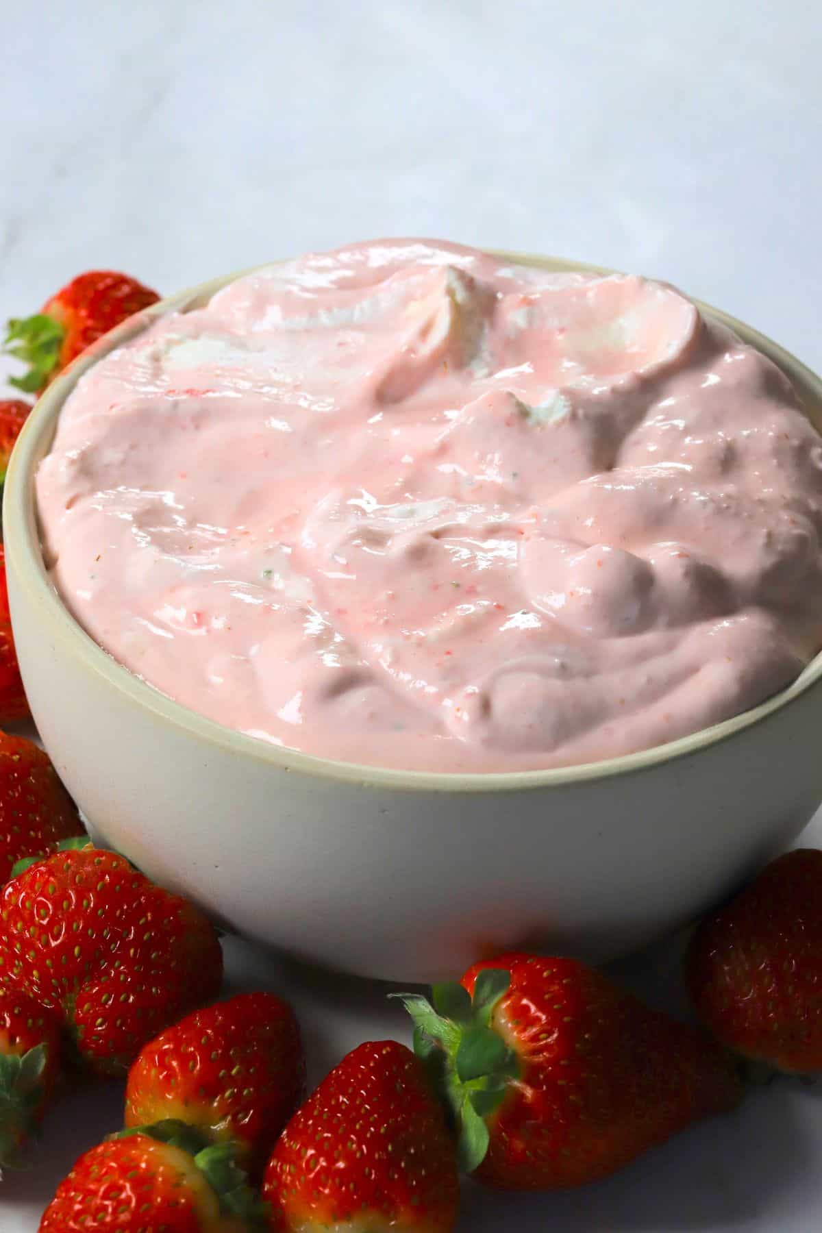High protein strawberry cheesecake fluff in a bowl and more strawberries surrounding the bowl.