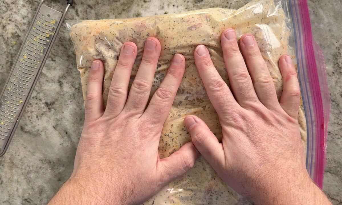 Smushing the chicken marinade in the freezer bag with hands.