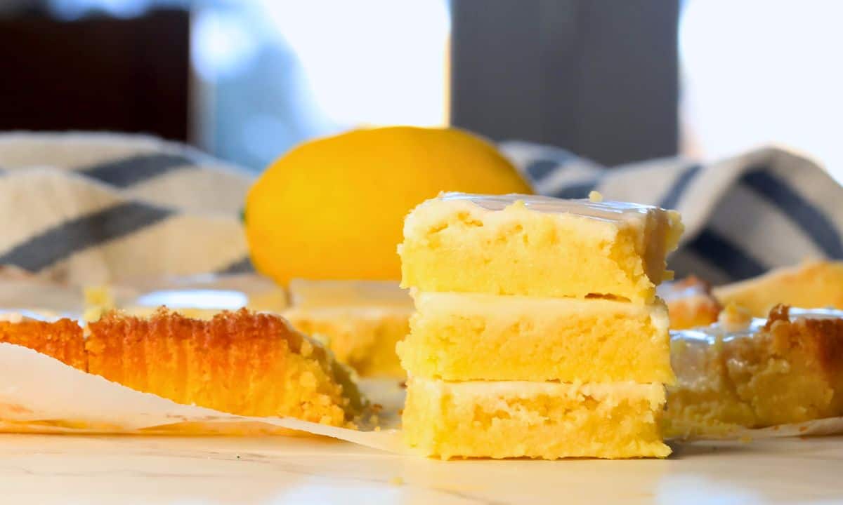 Three low carb lemon brownies stacked on top of each other with a lemon behind them.