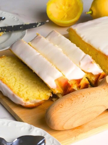 Sugar free lemon loaf slices on a cutting board next to lemons.