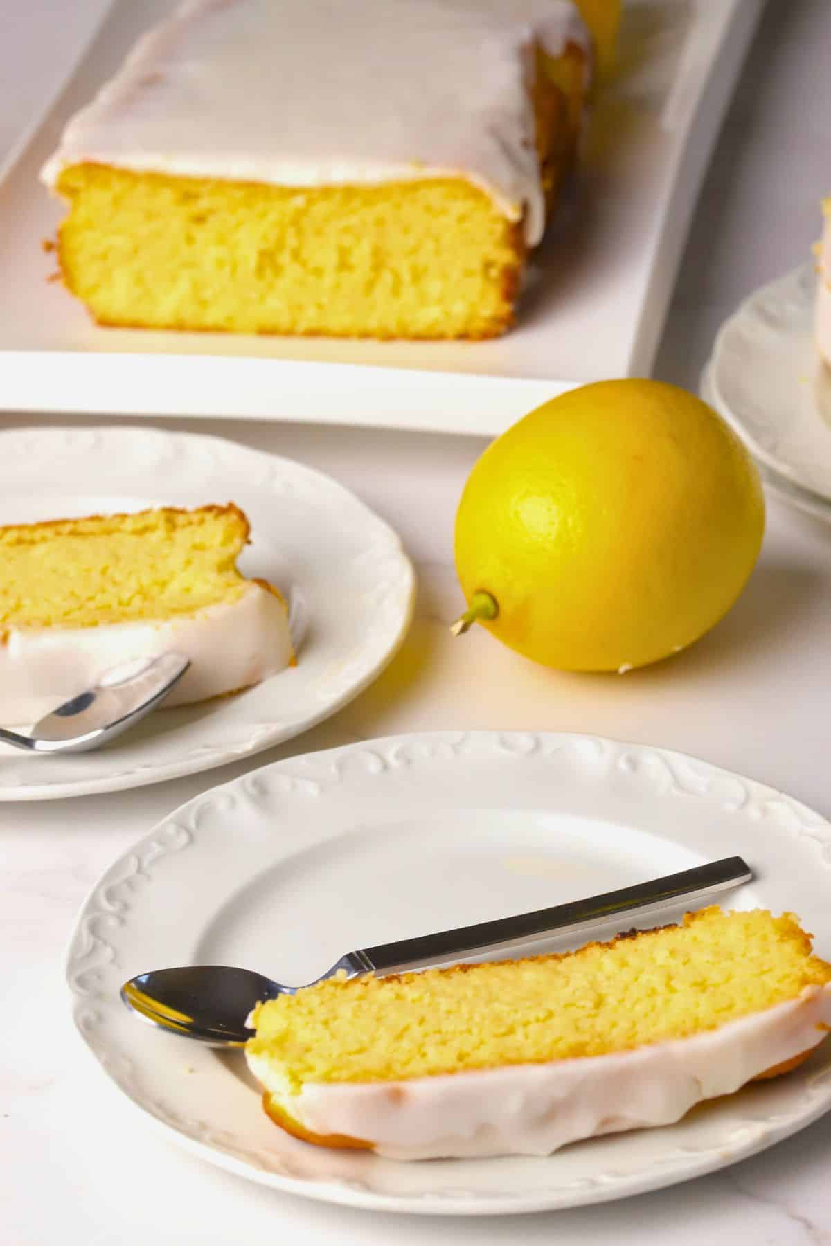 Sugar free lemon loaf slices on a cutting board next to some slices on plates and a lemon.