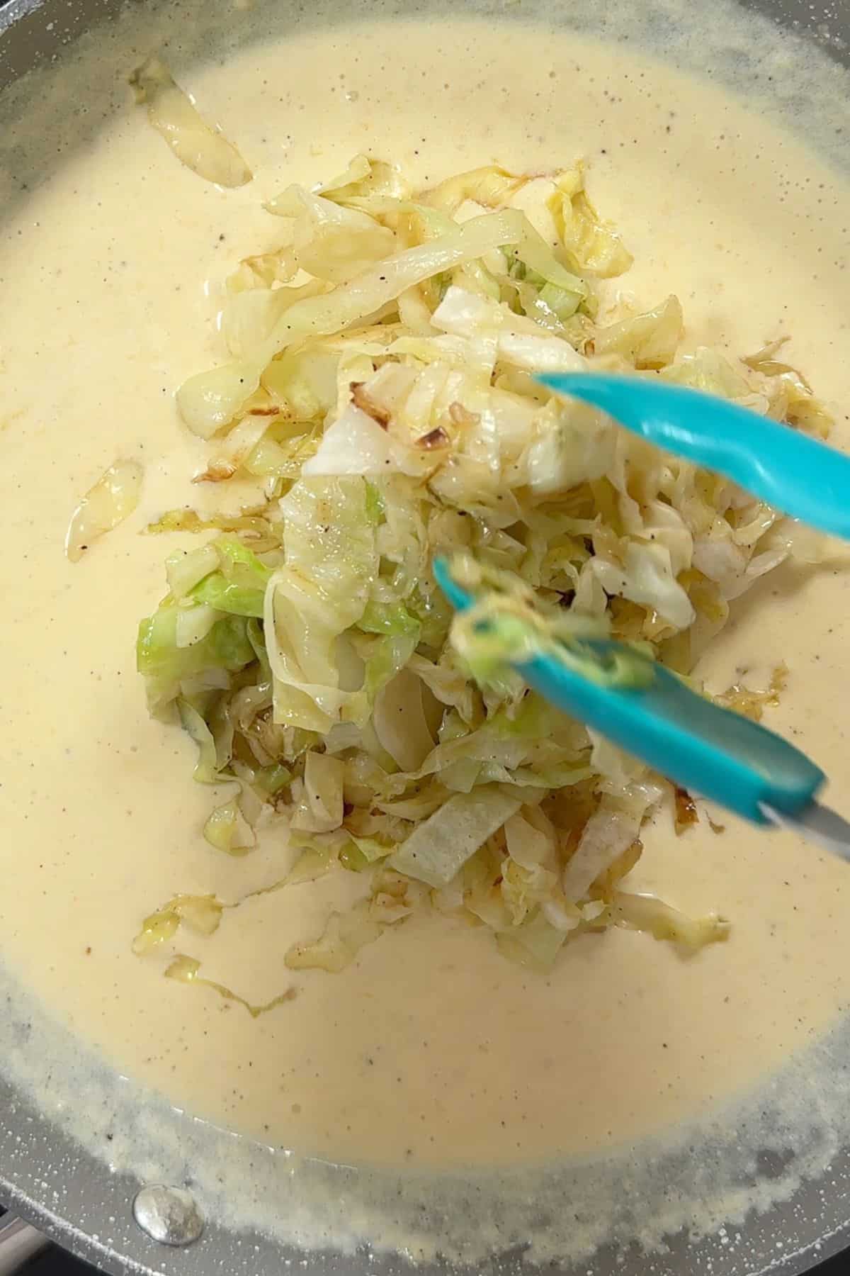 Adding the cabbage to the alfredo sauce.