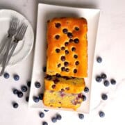 Low carb blueberry cottage cheese loaf cake on a platter next to some plates and forks.
