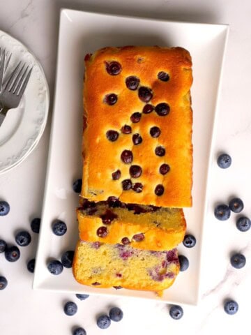 Low carb blueberry cottage cheese loaf cake on a platter next to some plates and forks.