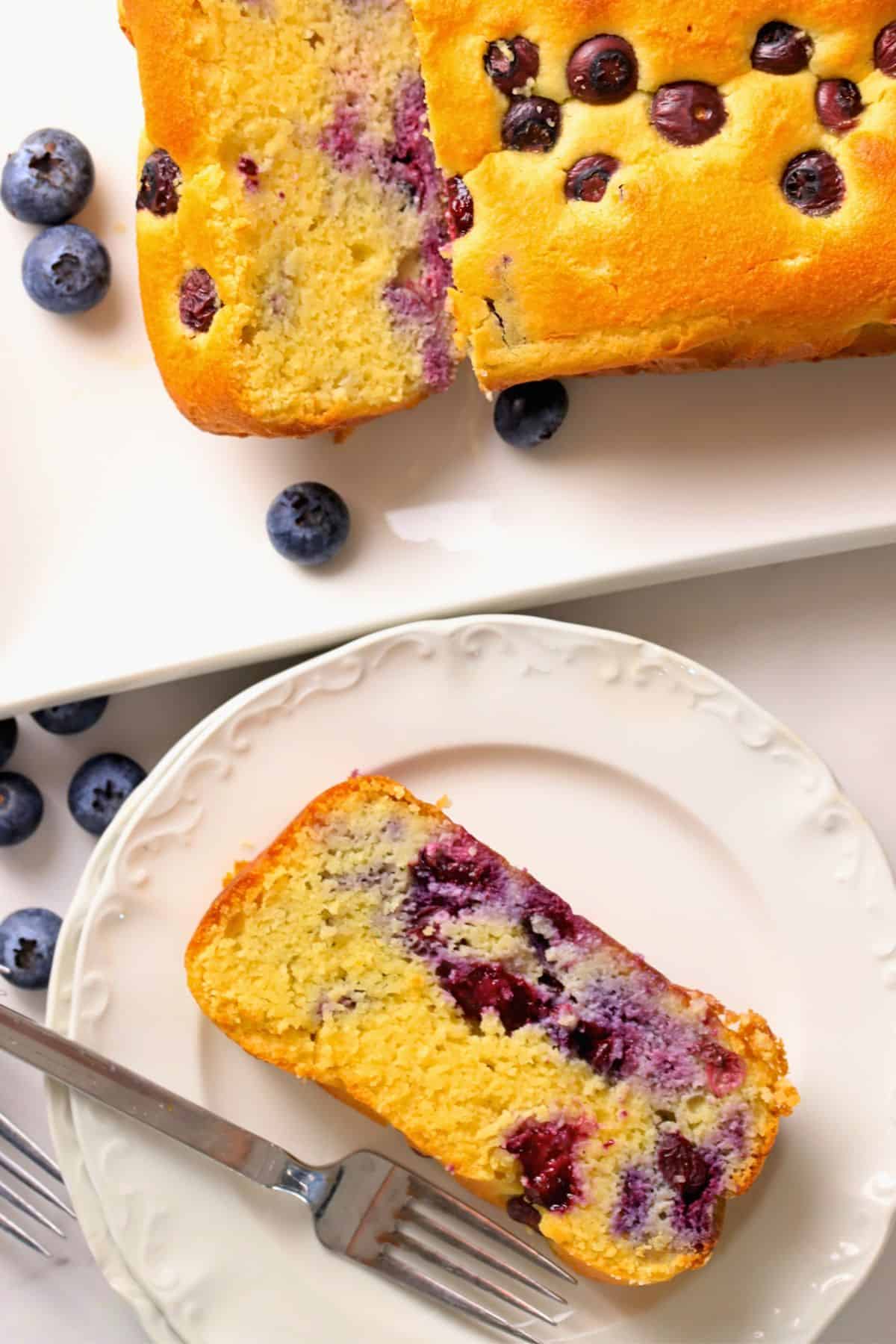 Low carb blueberry cottage cheese loaf cake on a platter next to a plate with a slice of cake.