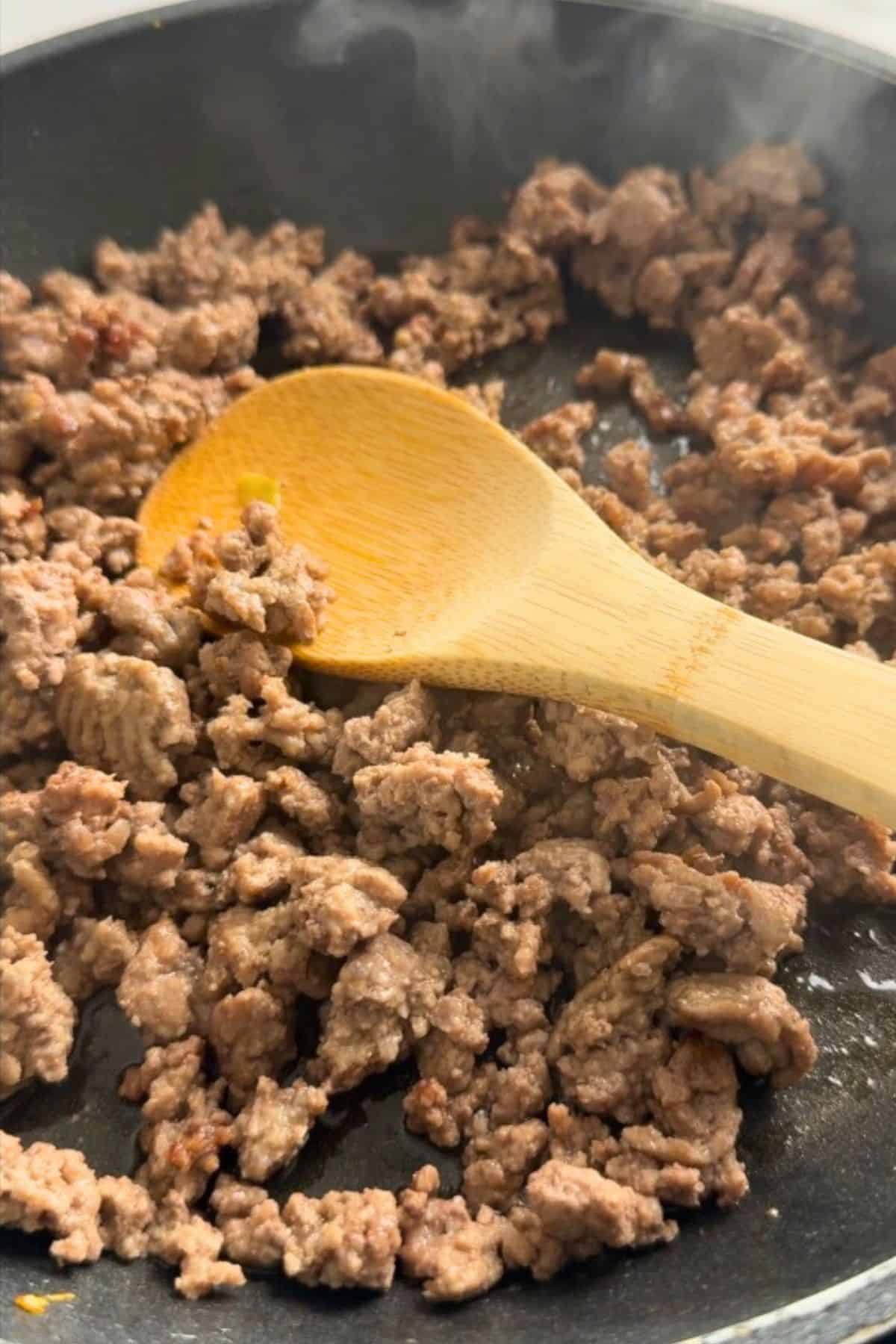 Browning the ground beef in a skillet with a wooden spoon.