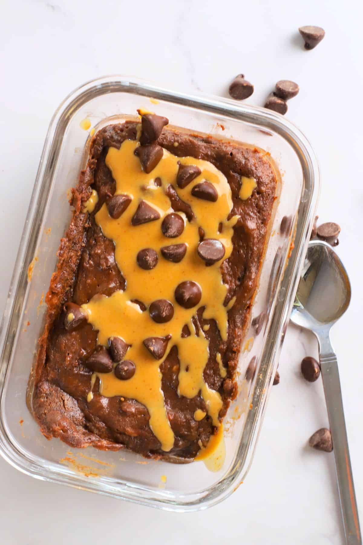 Cottage cheese chocolate protein mug cake drizzled with peanut butter and topped with chocolate chips and a spoon next to it.