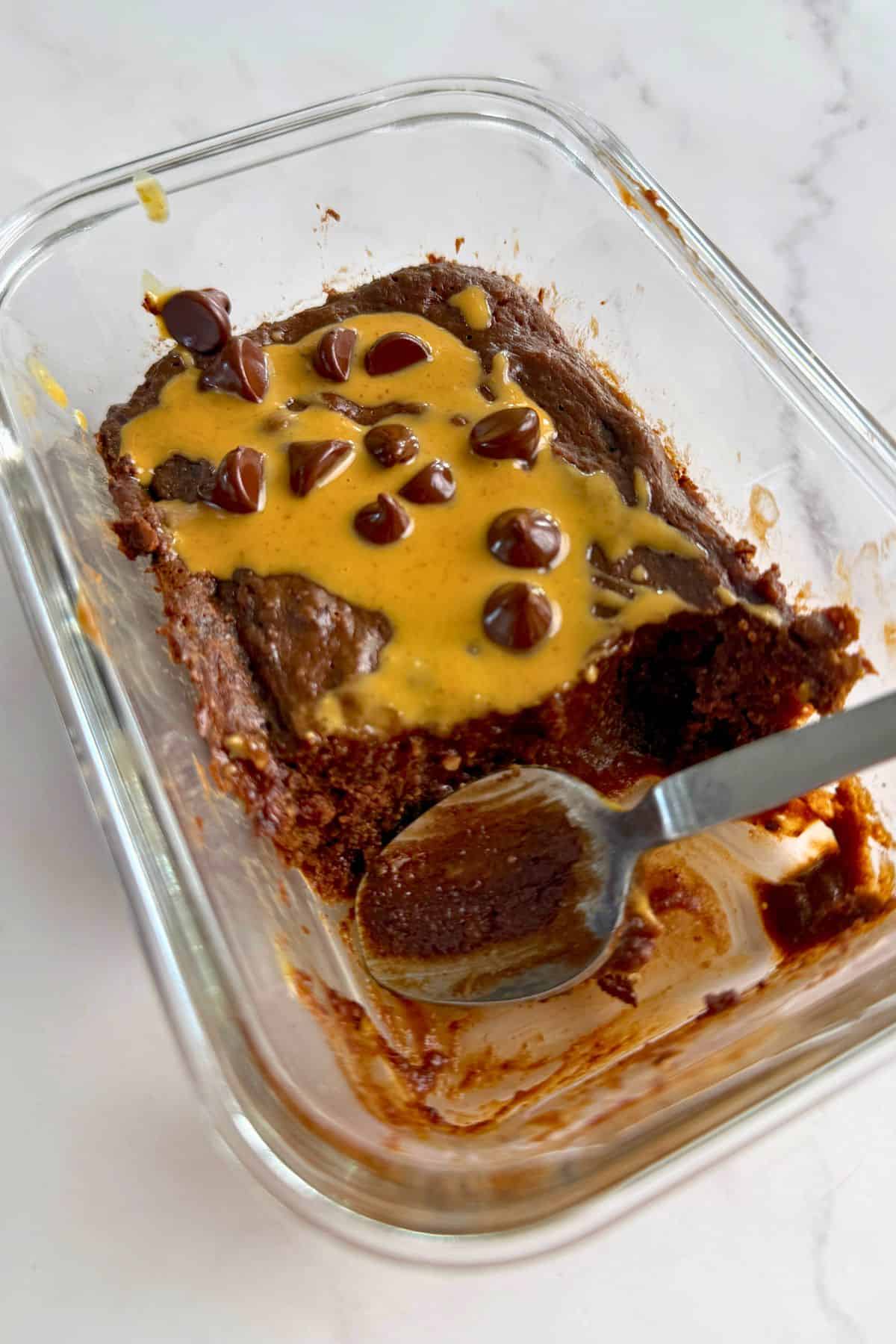 Cottage cheese chocolate protein mug cake drizzled with peanut butter and topped with chocolate chips with a spoon resting.