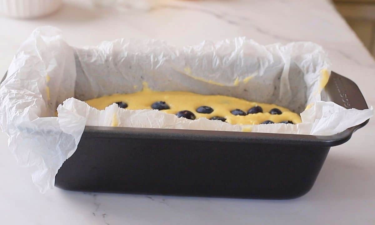 Loaf pan with cake batter topped with blueberries.