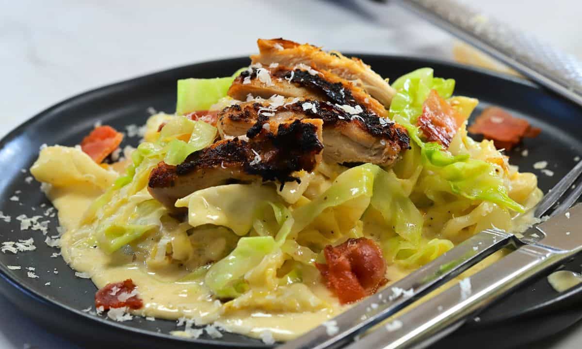 Wide shot of low carb cabbage alfredo with chicken and bacon on a plate.