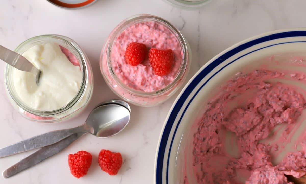 Low carb raspberry chia pudding in a mason jar topped with fresh raspberries next to a bowl with the same.