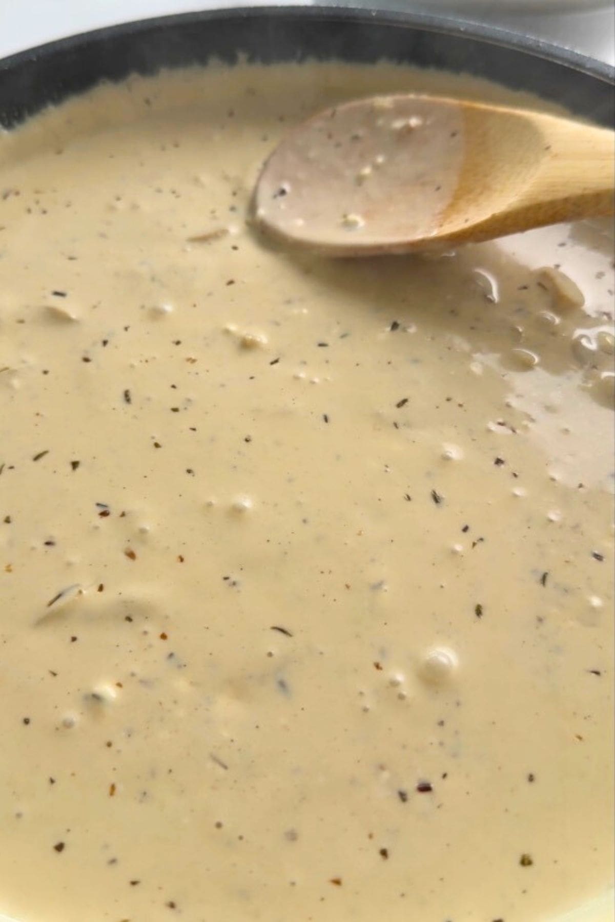Creamy sauce in a skillet with a wooden spoon.