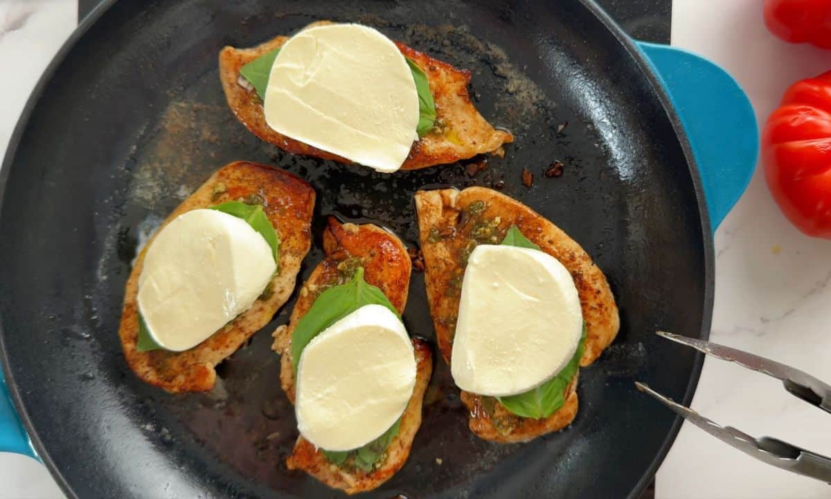 Chicken in the skillet topped with the fresh basil and fresh mozzarella.