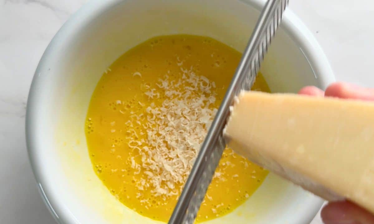 Shredding parmesan over the sauce in a bowl.