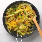 Low carb cabbage carbonara in a pan with a wooden spoon.