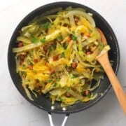 Low carb cabbage carbonara in a pan with a wooden spoon.
