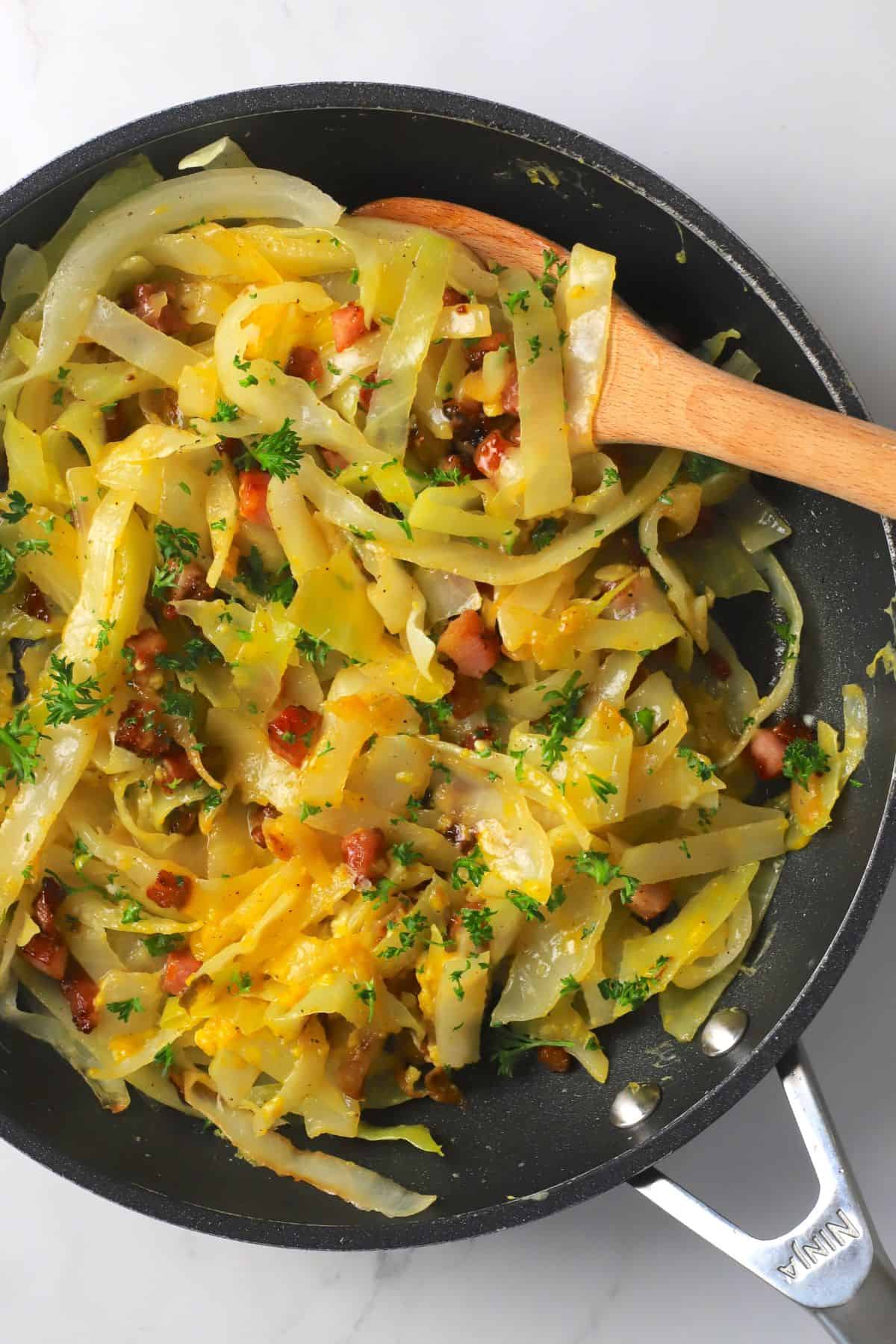 Low carb cabbage carbonara in a pan with a wooden spoon.