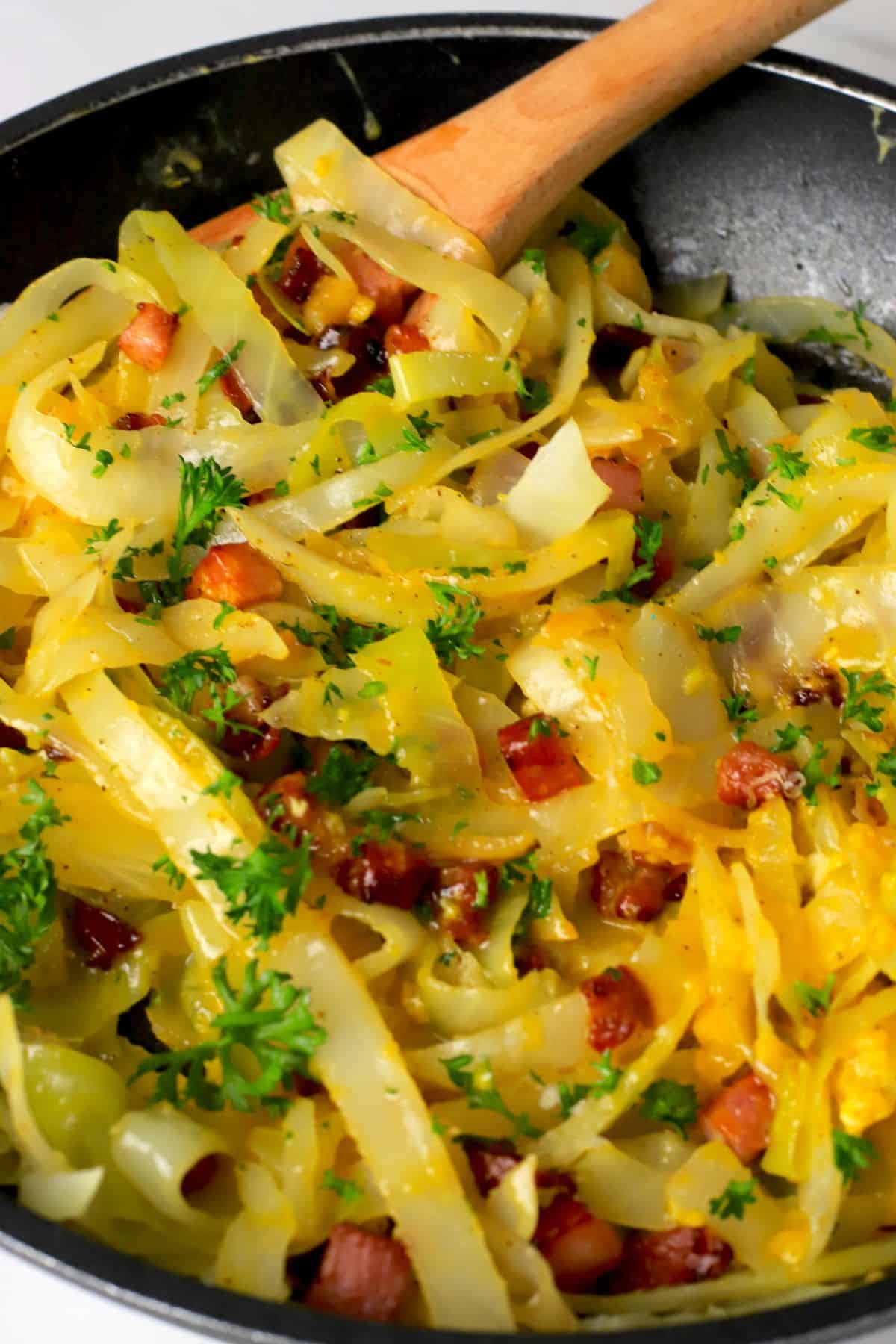 Low carb cabbage carbonara in a pan with a wooden spoon.