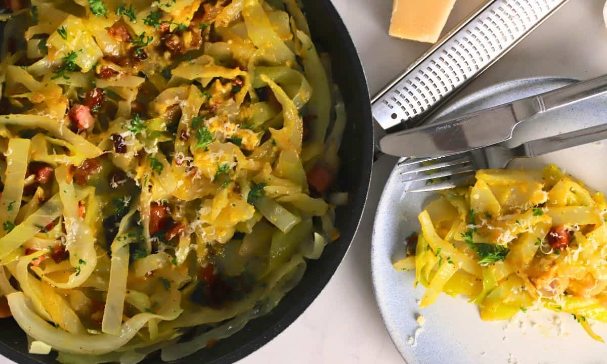 Low carb cabbage carbonara in a pan with a wooden spoon next to a plate with the same.