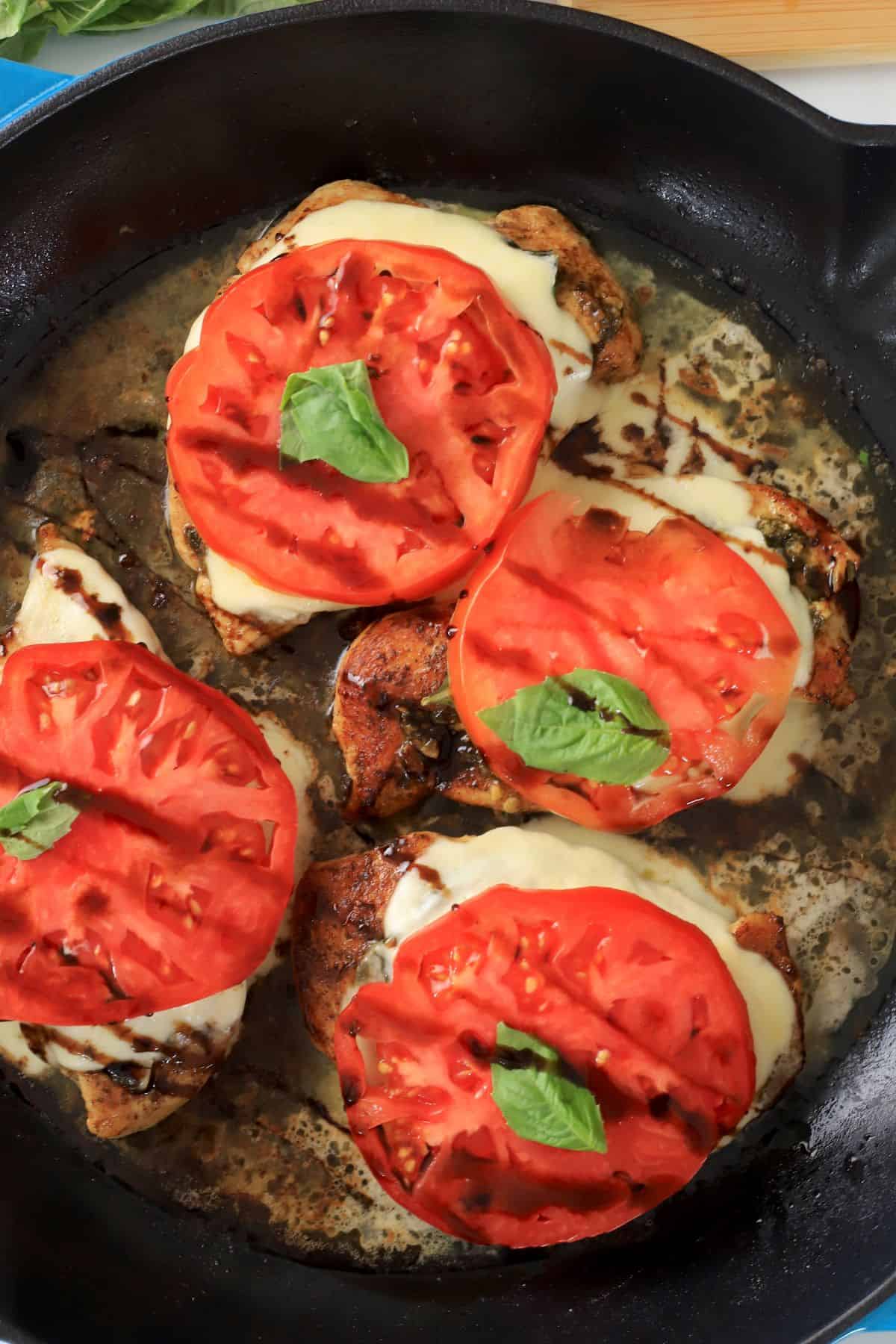 Low carb pesto caprese chicken in a skillet topped with fresh basil.