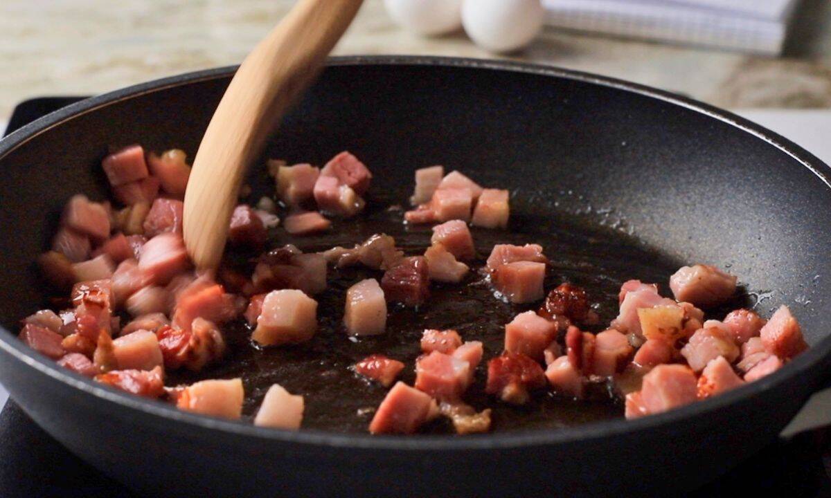 Cubed pancetta frying in a skillet.