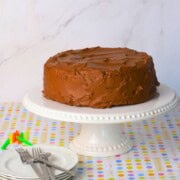 Diabetic chocolate birthday cake on a cake stand with candles, plates and forks.