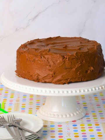 Diabetic chocolate birthday cake on a cake stand with candles, plates and forks.