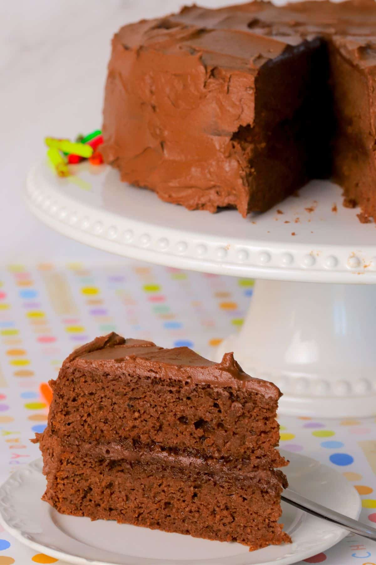 Diabetic chocolate birthday cake on a cake stand with a slice of cake on a plate.