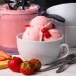 Low carb strawberry cottage cheese ice cream in a bowl with strawberries and the ninja creami pint next to the bowl.