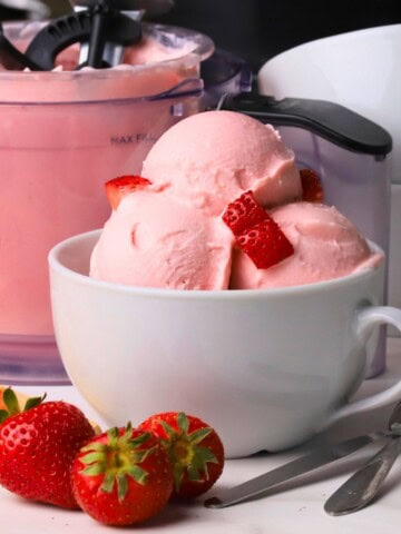 Low carb strawberry cottage cheese ice cream in a bowl with strawberries and the ninja creami pint next to the bowl.