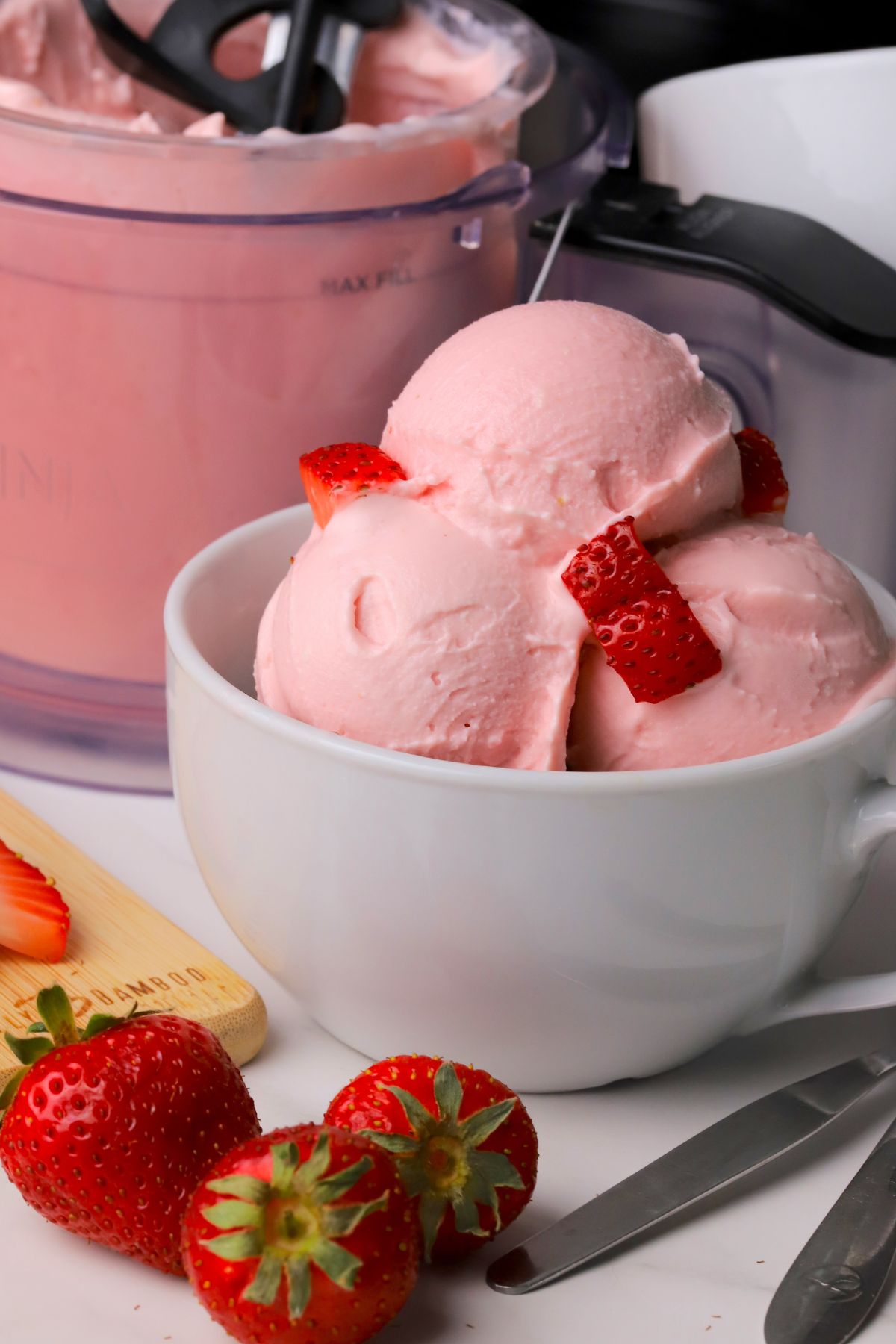 Low carb strawberry cottage cheese ice cream in a bowl with strawberries and the ninja creami pint next to the bowl.